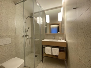 Ein modernes Badezimmer mit einer Duschkabine aus Glas, einem Holzbadezimmer-Möbelkorpus mit Waschbecken und einem Spiegel darüber.