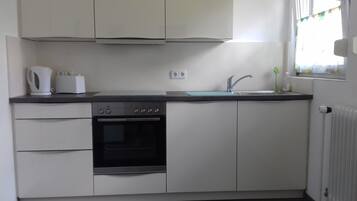 Eine kleine Küche mit integriertem Backofen, Spüle und Wasserkocher auf der Arbeitsfläche.