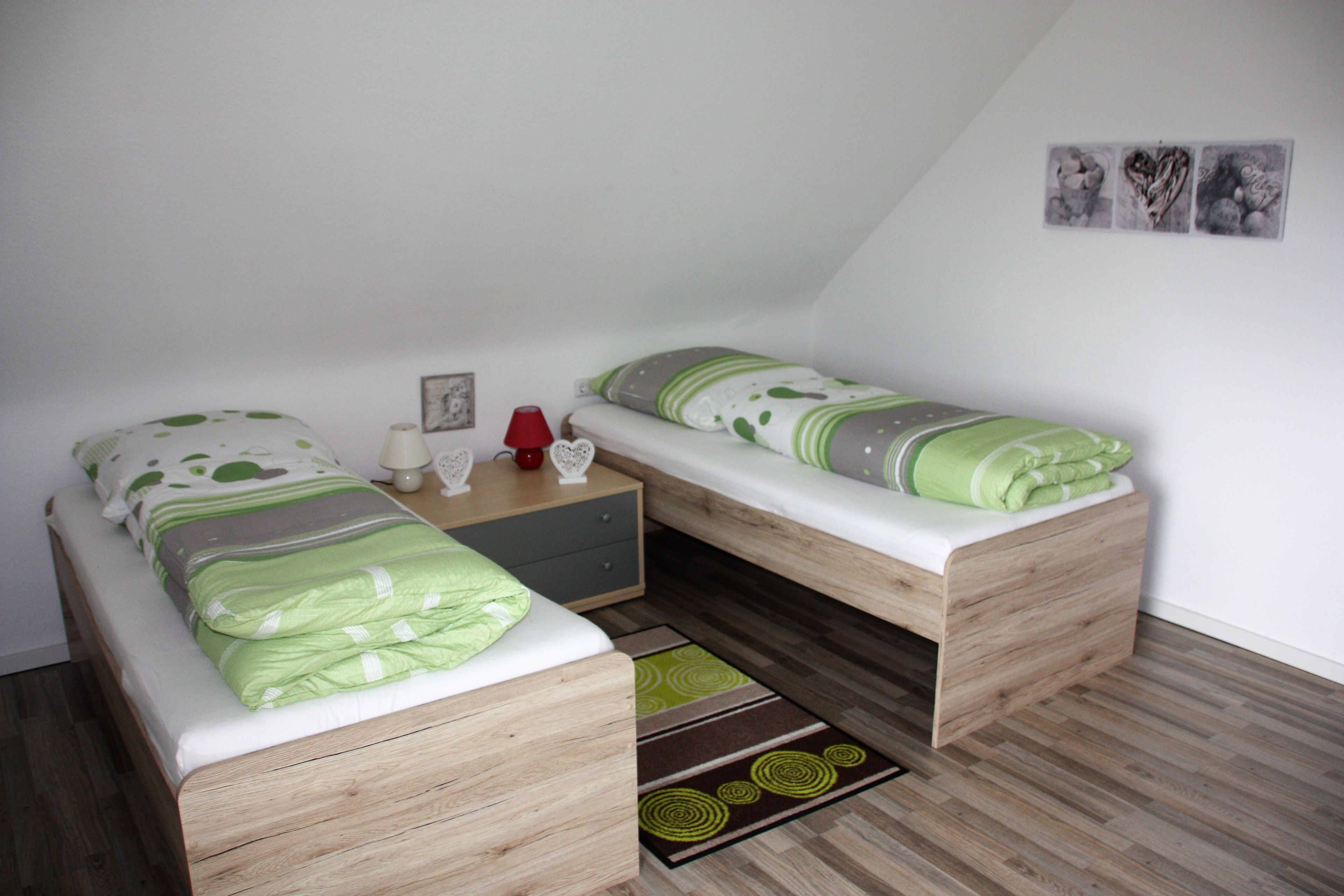 Ein kleines, gemütliches Schlafzimmer mit zwei Einzelbetten, einem Nachttisch, einer Lampe und einem kleinen Tisch.