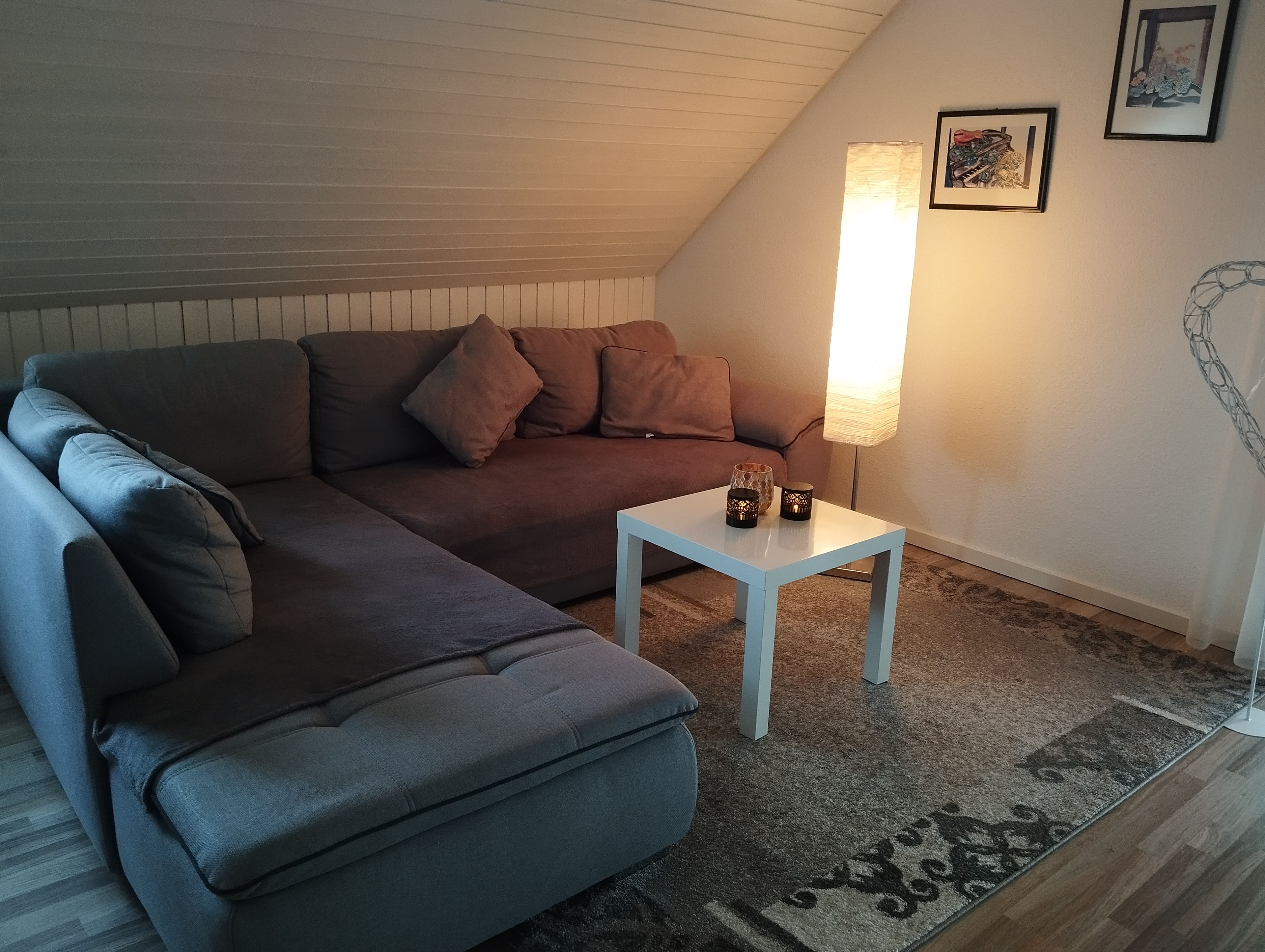 Ein gemütliches Wohnzimmer mit einem Ecksofa, einem kleinen weißen Tisch und einer Stehlampe.