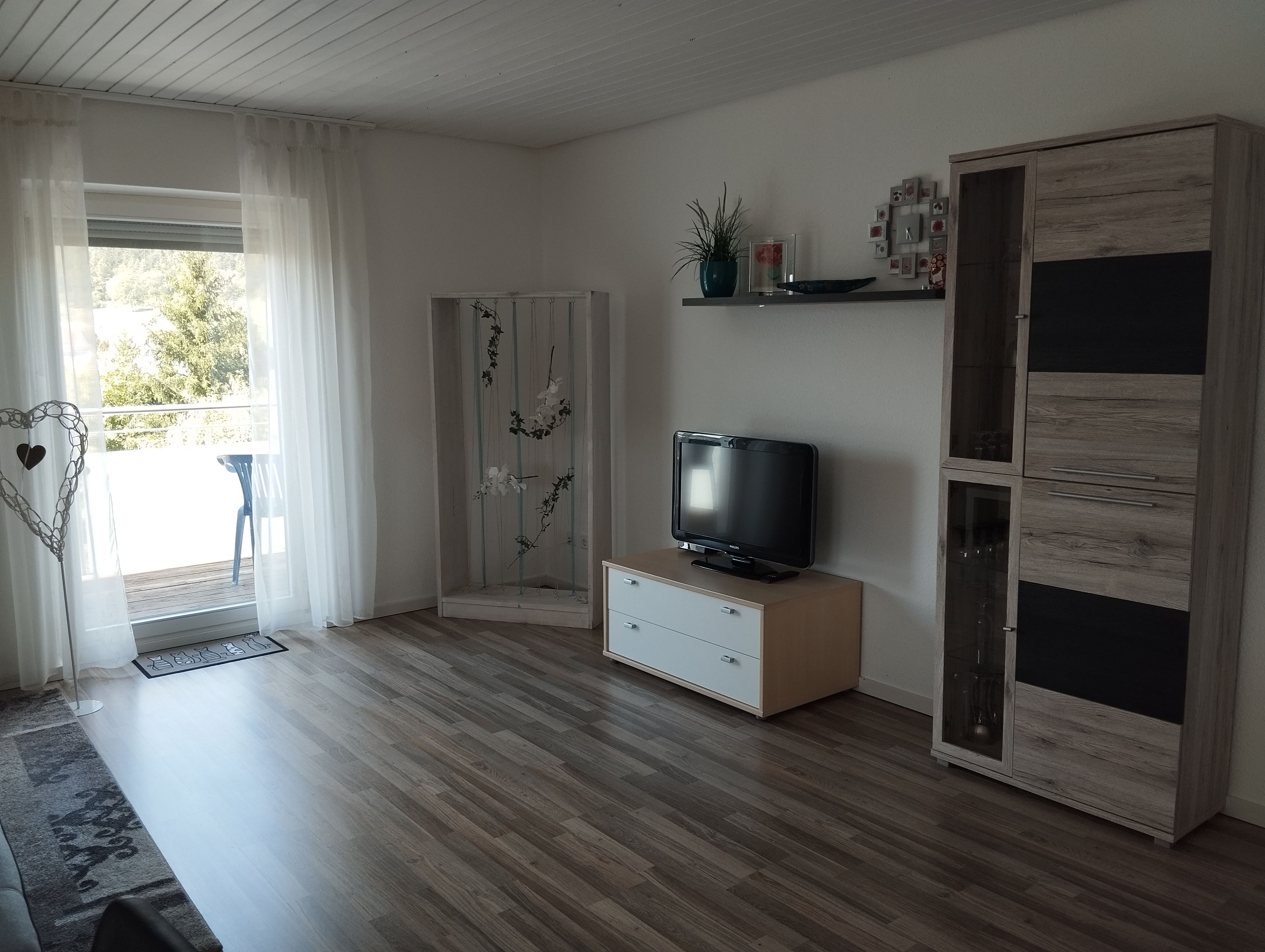 Ein modernes Wohnzimmer mit Flachbildfernseher, Holzboden, einer Schiebetür aus Glas und einer eingebauten Vitrine.