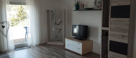 Una sala de estar moderna con televisor de pantalla plana, piso de madera, puerta corredera de vidrio y mueble empotrado.