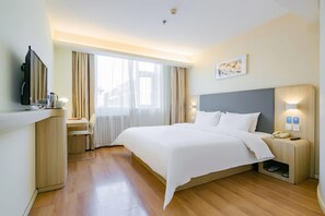 Una habitación de hotel con una cama, mesita de noche, lámpara y televisor sobre un mueble.
