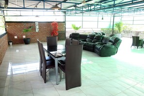 Un espacio de estar al aire libre cubierto con pared de ladrillo, una mesa de vidrio y sofás con cojines verdes.
