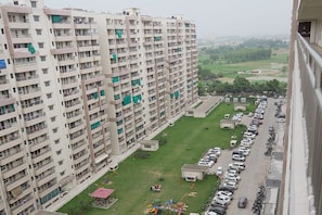 Un immeuble résidentiel de grande hauteur doté de nombreux balcons, d’un parking et d’un petit espace de jeux pour enfants.