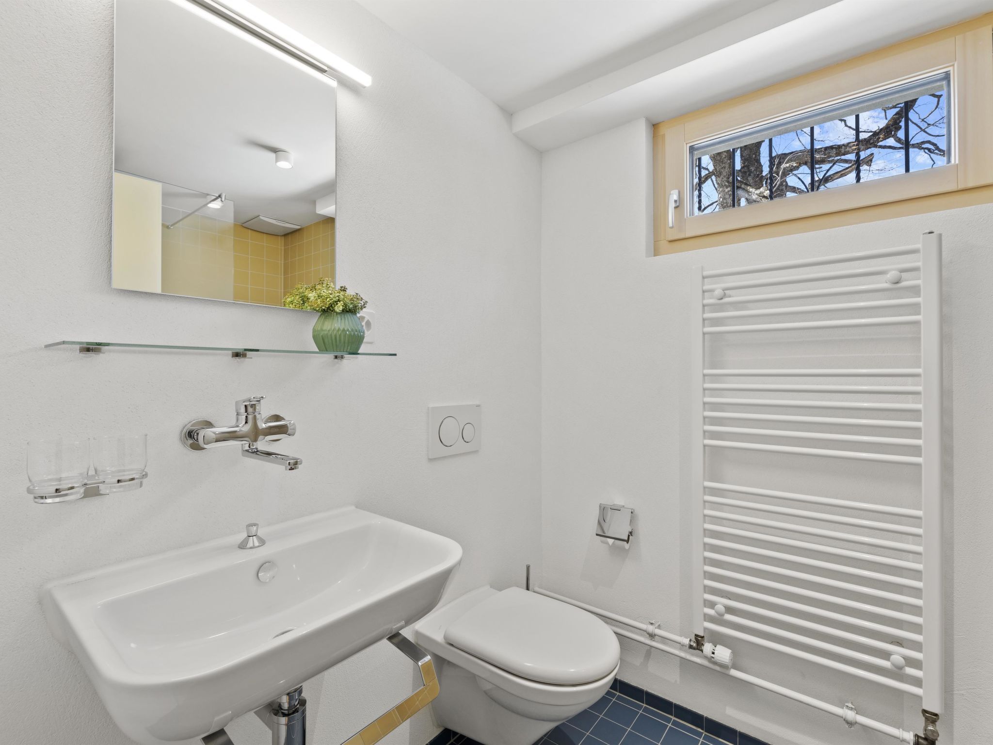 A modern bathroom with a white sink, mirror, and toilet.