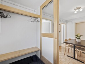 Ein modernes Zimmer mit einer Holzbank, einem Kleiderständer, einem Esstisch mit Stühlen und einer Topfpflanze.