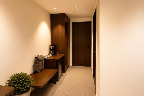 A hallway with a wooden bench, a small table with a coffee maker, and a door at the end.