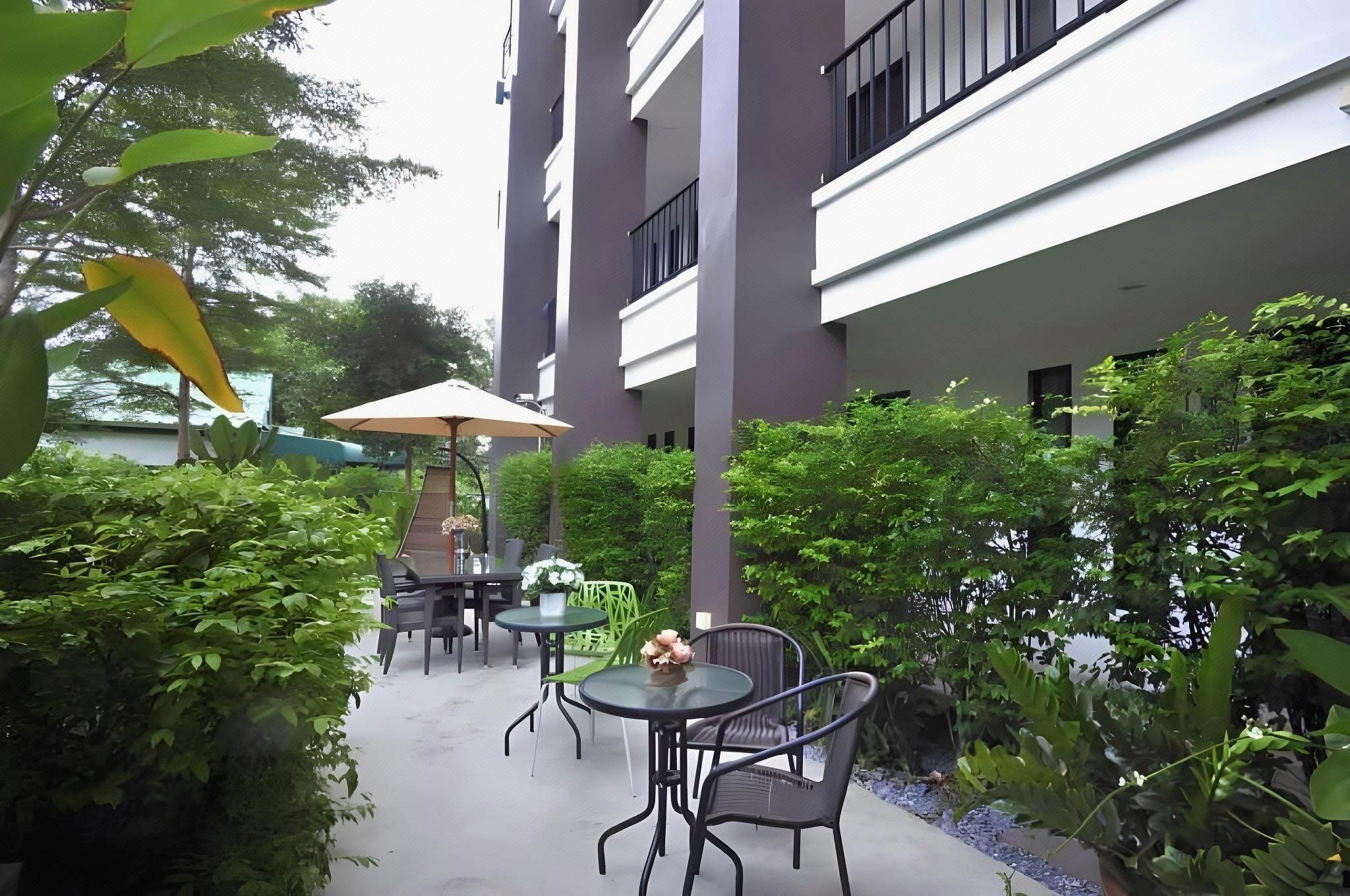 An outdoor patio area with tables and chairs, surrounded by greenery and a building with balconies.