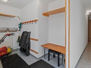 Ein kleines Zimmer mit einem Holztisch, einem Stuhl, einem roten Rasenmäher und einer Wandhalterung zum Wäschetrocknen.