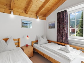 Ein Schlafzimmer mit zwei Betten, einem Nachttisch, einer Lampe und einem Fenster mit Vorhängen.