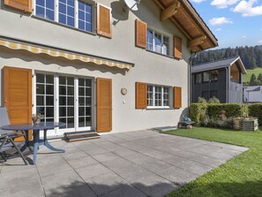 Ein zweistöckiges Haus mit einer Terrasse, Holzklappläden und einem Garten.