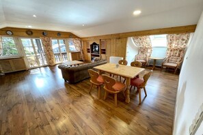 Ein geräumiges Zimmer mit Holzboden, einem Esstisch mit Stühlen, einer Couch und einem Fernseher.
