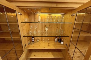 Ein Holzschrank mit Glastüren, der Weingläser und Flaschen beherbergt.