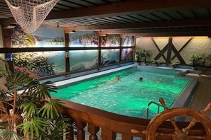 Ein Innenpool mit Blick auf einen Wasserfall und üppige tropische Pflanzen.