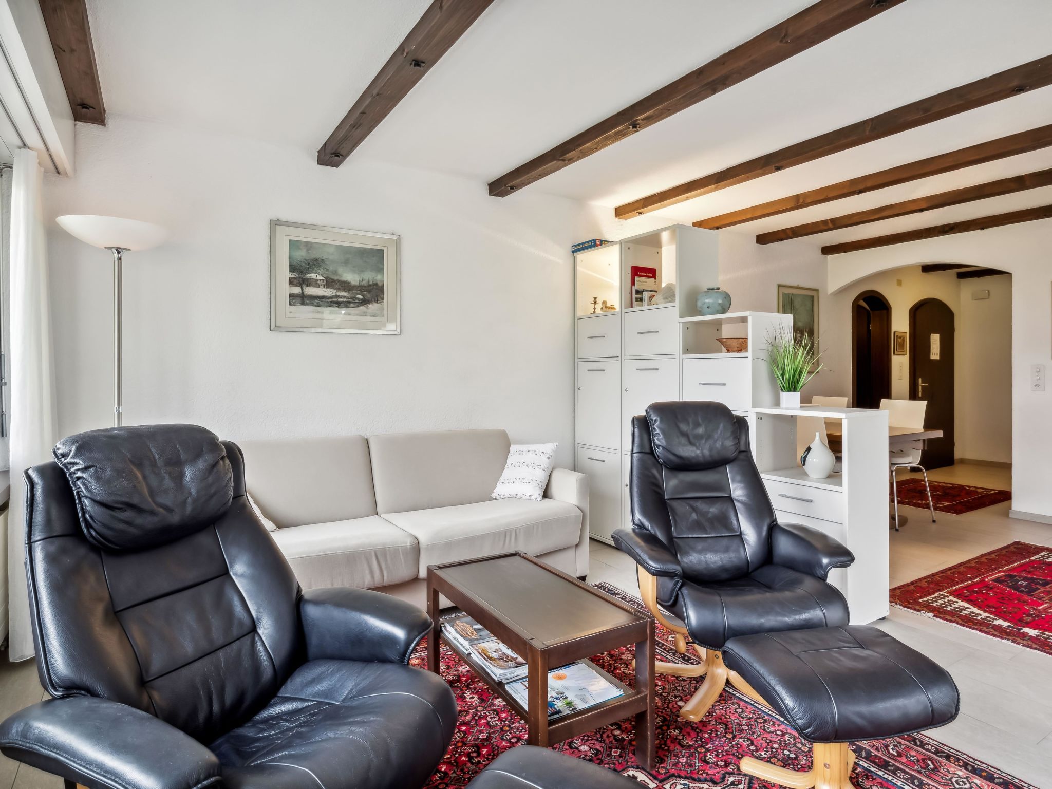 Ein modernes Wohnzimmer mit einer Couch, zwei Ledersesseln, einem Couchtisch und einem Bücherregal.