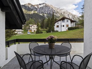 Eine Terrasse mit rundem Tisch und Stühlen, einem Blumentopf und Blick auf die Berge.