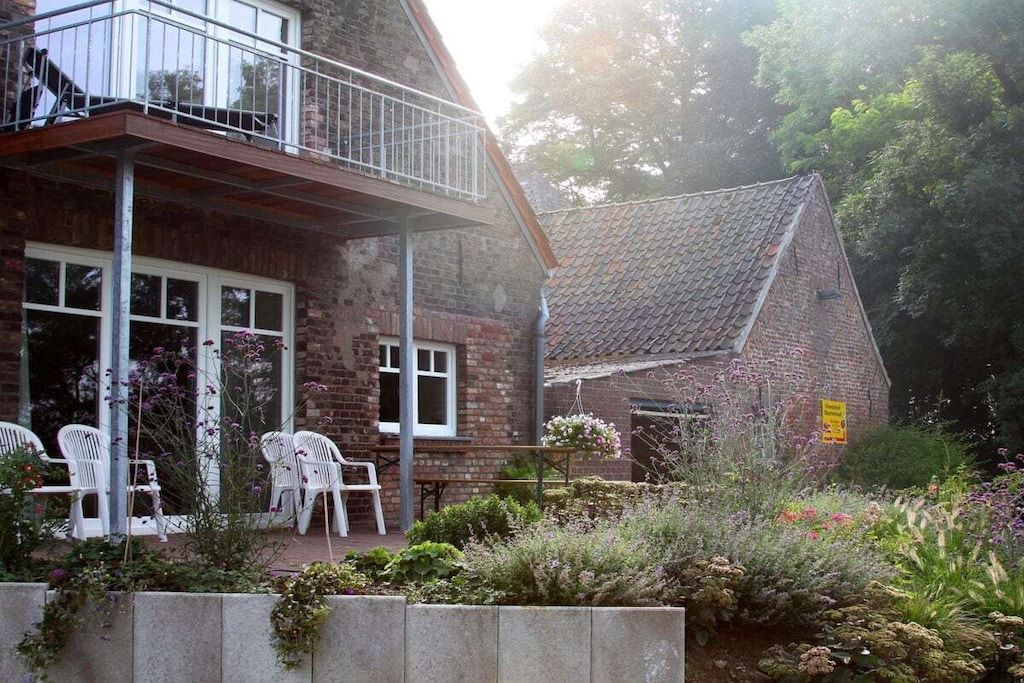 A two-story house with a balcony, a garden with various plants, and outdoor seating.