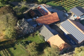 An aerial view of a property with multiple buildings, including a large structure with a sloped roof and solar panels, surrounded by trees and open fields. - Holiday apartment in Rees with swimming pool (Rees)