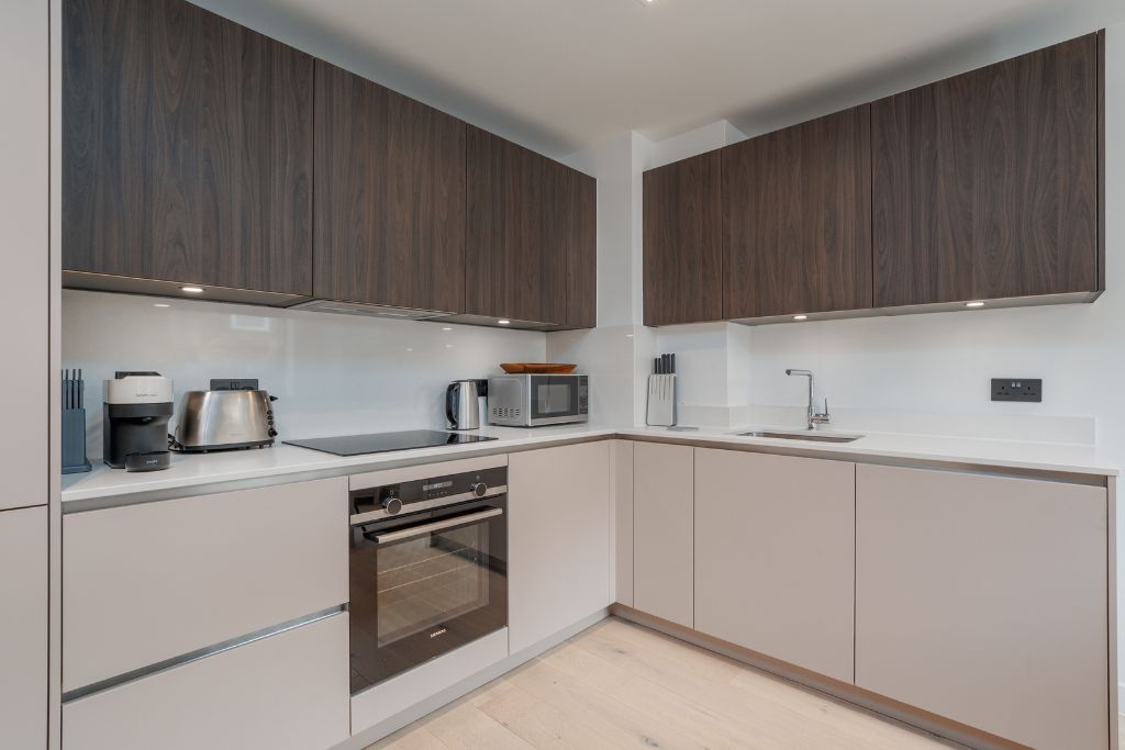 Een moderne keuken met donkere houtkasten, roestvrijstalen apparatuur en een wit aanrecht.
