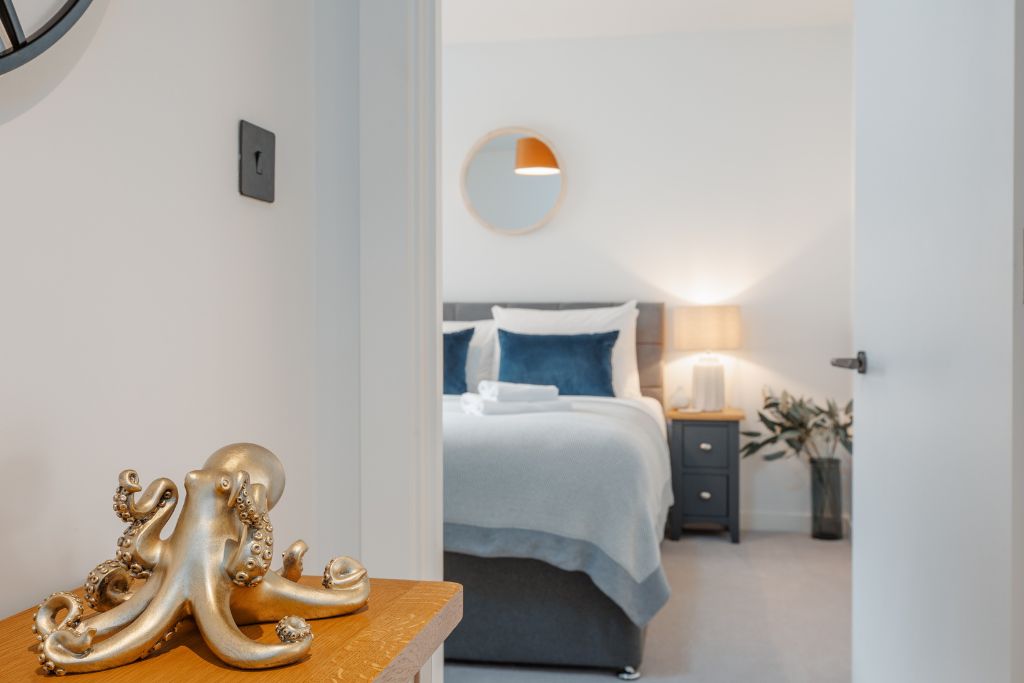 Habitación de hotel con cama, mesita de noche, lámpara y una escultura decorativa de pulpo sobre una superficie de madera.