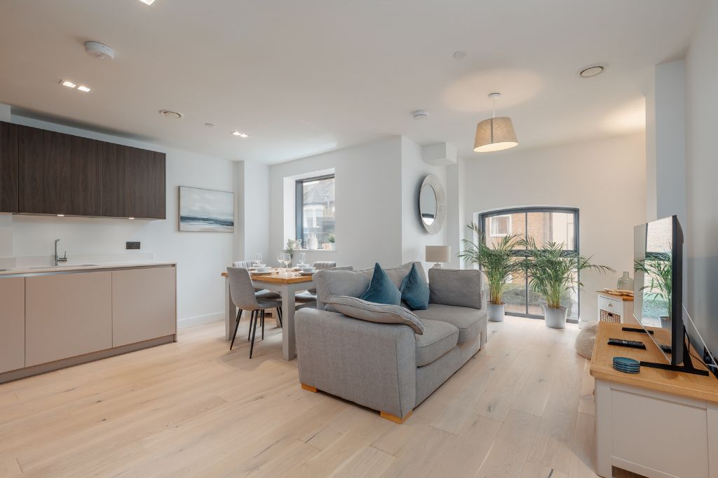 A modern living space with a sofa, dining area, kitchen, and large windows.