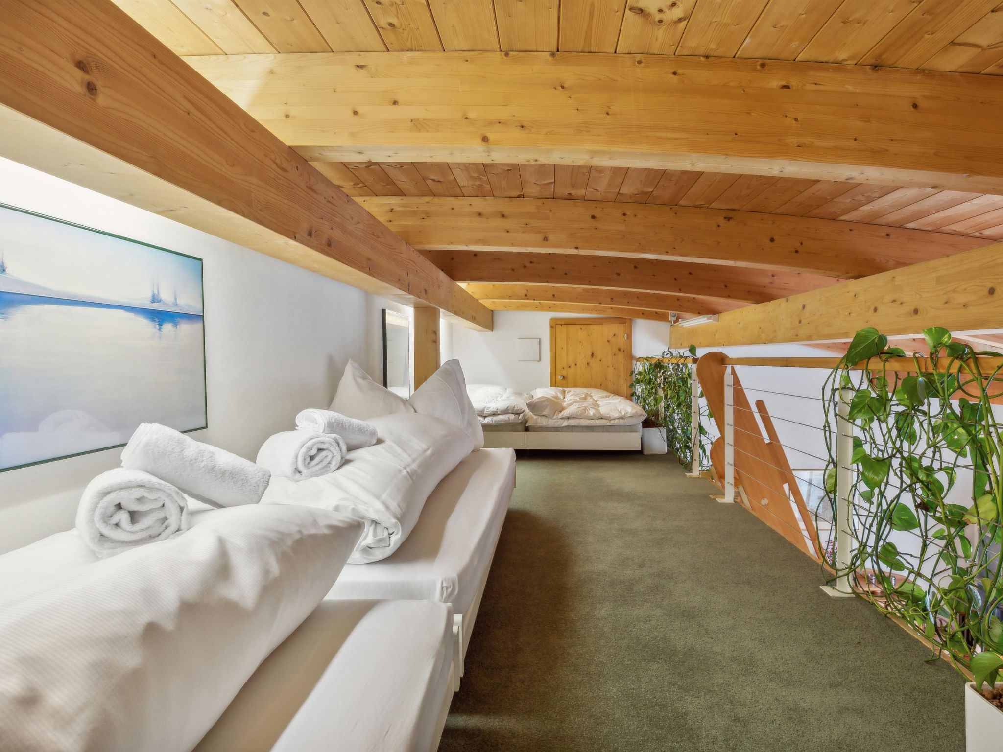 Habitación de hotel con techo de madera, cama con ropa blanca, un cuadro en la pared y una planta junto a la ventana.