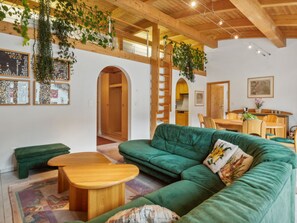Un salon chaleureux avec un canapé vert, une table basse en bois et un escalier menant à une mezzanine agrémentée de plantes.