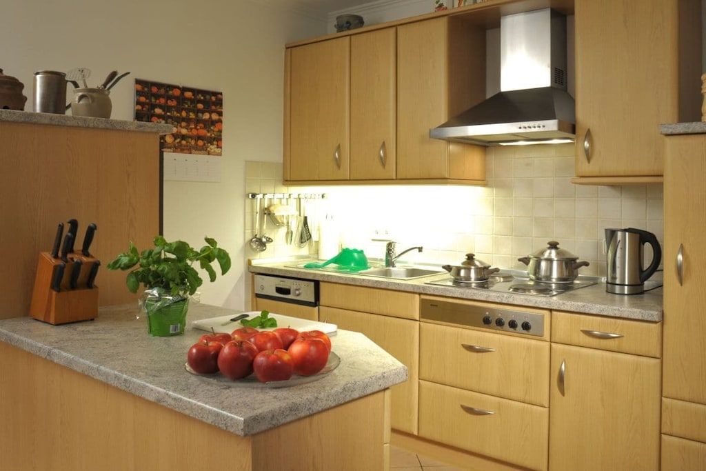 Een keuken met houten kastjes, een roestvrijstalen afzuigkap en een aanrecht met een kom tomaten.