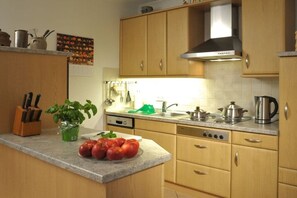 Cozinha com armários de madeira, exaustor de aço inoxidável e bancada com uma tigela de tomates.