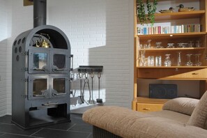 Een moderne woonkamer met een zwarte houtkachel, een boekenkast met boeken en glazen, en een comfortabele bank.