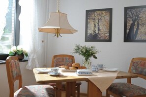Ein Essbereich mit einem Tisch für zwei Personen, Stühlen mit gemusterten Bezügen, einer Hängeleuchte und gerahmten Kunstwerken an der Wand.