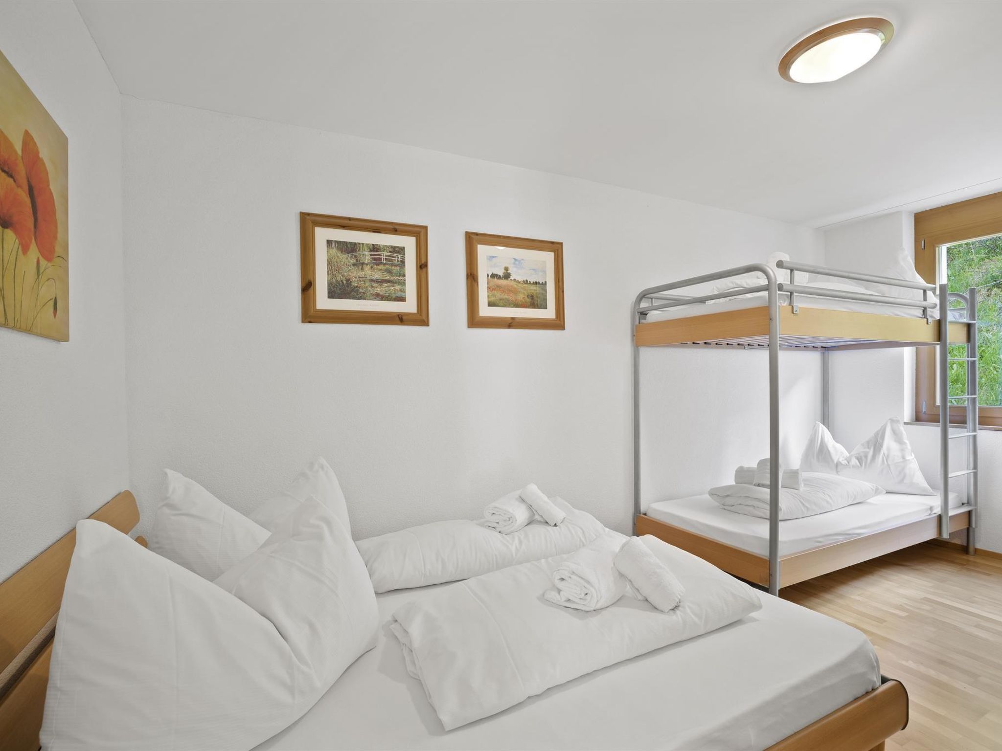 A room with a bunk bed, a single bed, and two framed pictures on the wall.