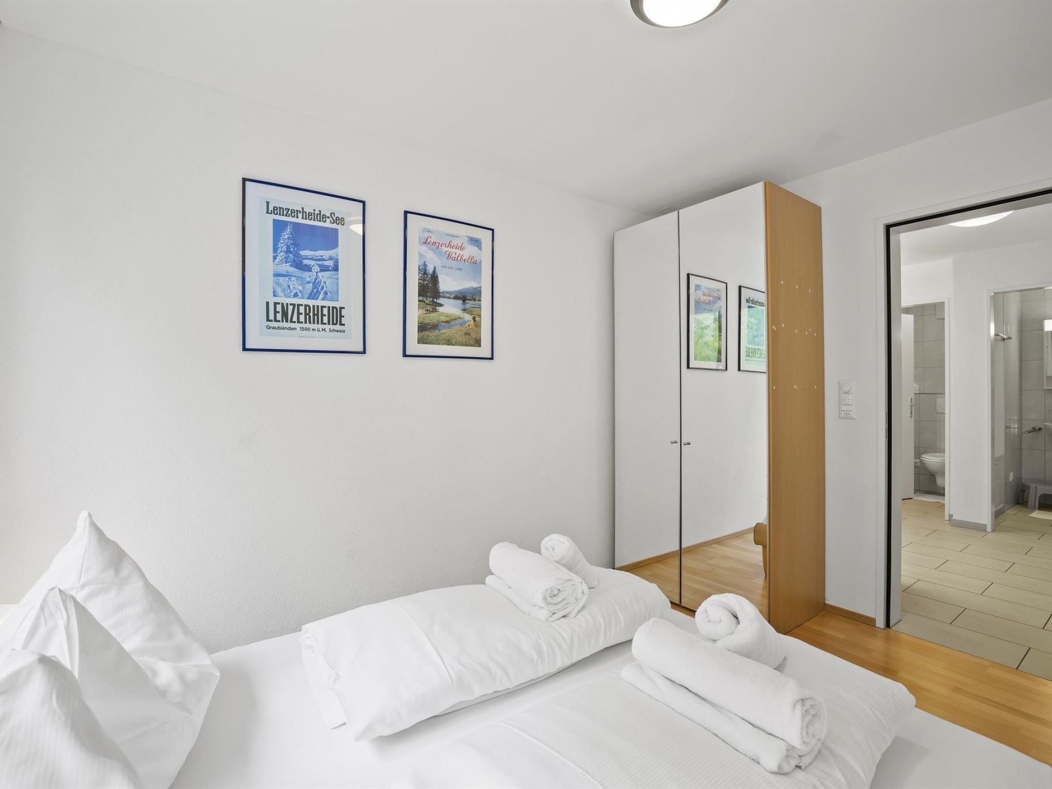 Habitación de hotel con cama, toallas blancas, un armario y dos cuadros en la pared.
