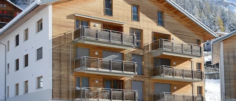 Un immeuble en bois à plusieurs étages, doté de balcons, d’une entrée couverte et offrant une vue sur des arbres couverts de neige.
