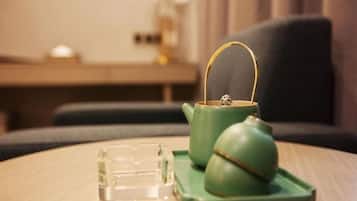 Een groene theepot en kopje op een tafel, met een glazen vaas ernaast.