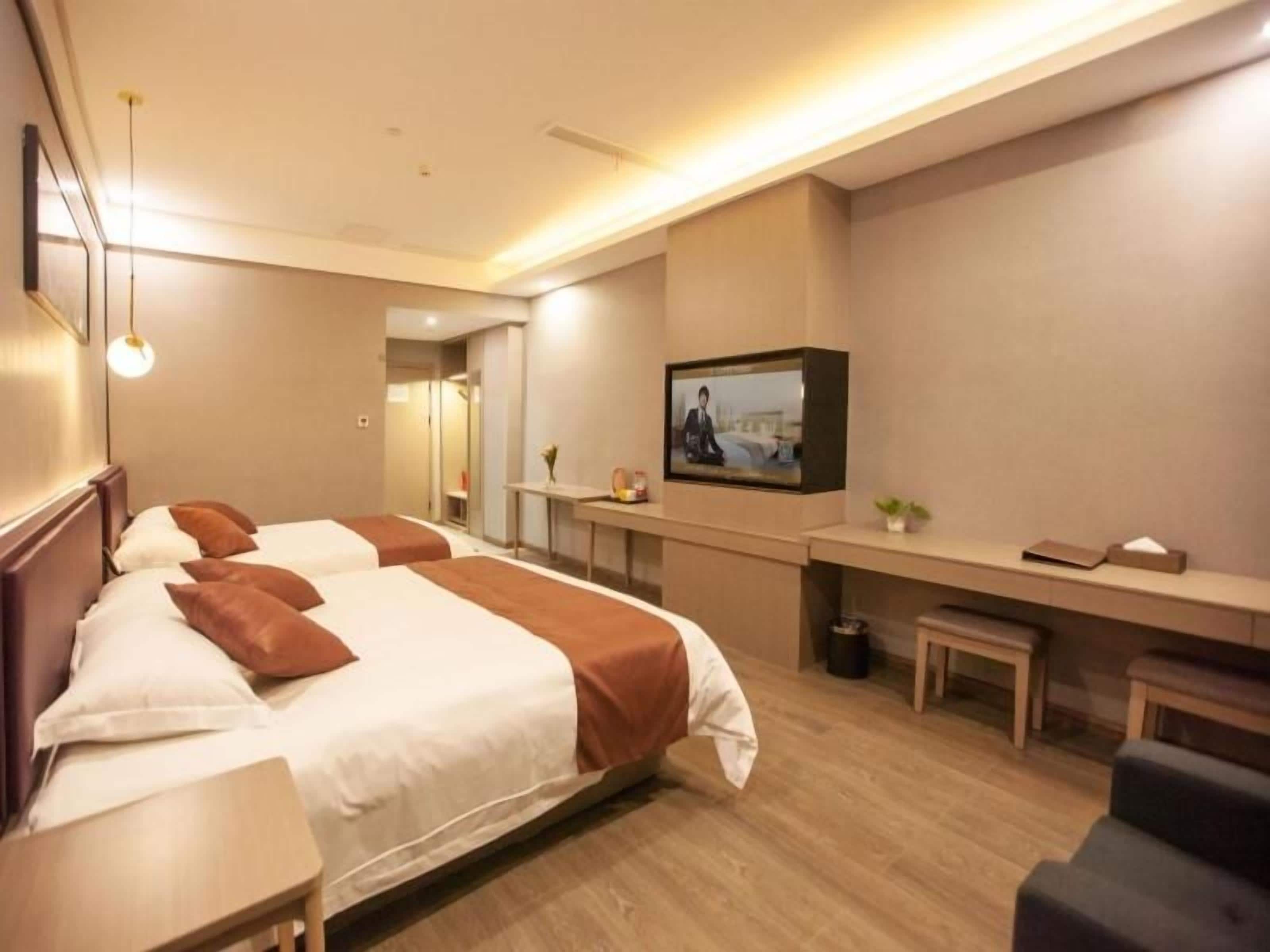 Habitación de hotel con dos camas, un escritorio, un televisor y una pequeña zona de estar.