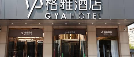 Het exterieur van GYA HOTEL, met een moderne gevel, grote glazen entree deuren en een vogel logo boven de naam.