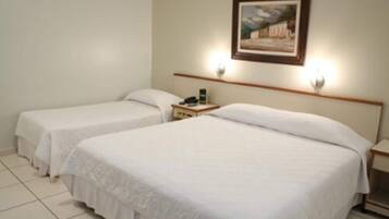 Quarto de hotel com duas camas de solteiro, uma mesa de cabeceira com abajur e um quadro na parede.
