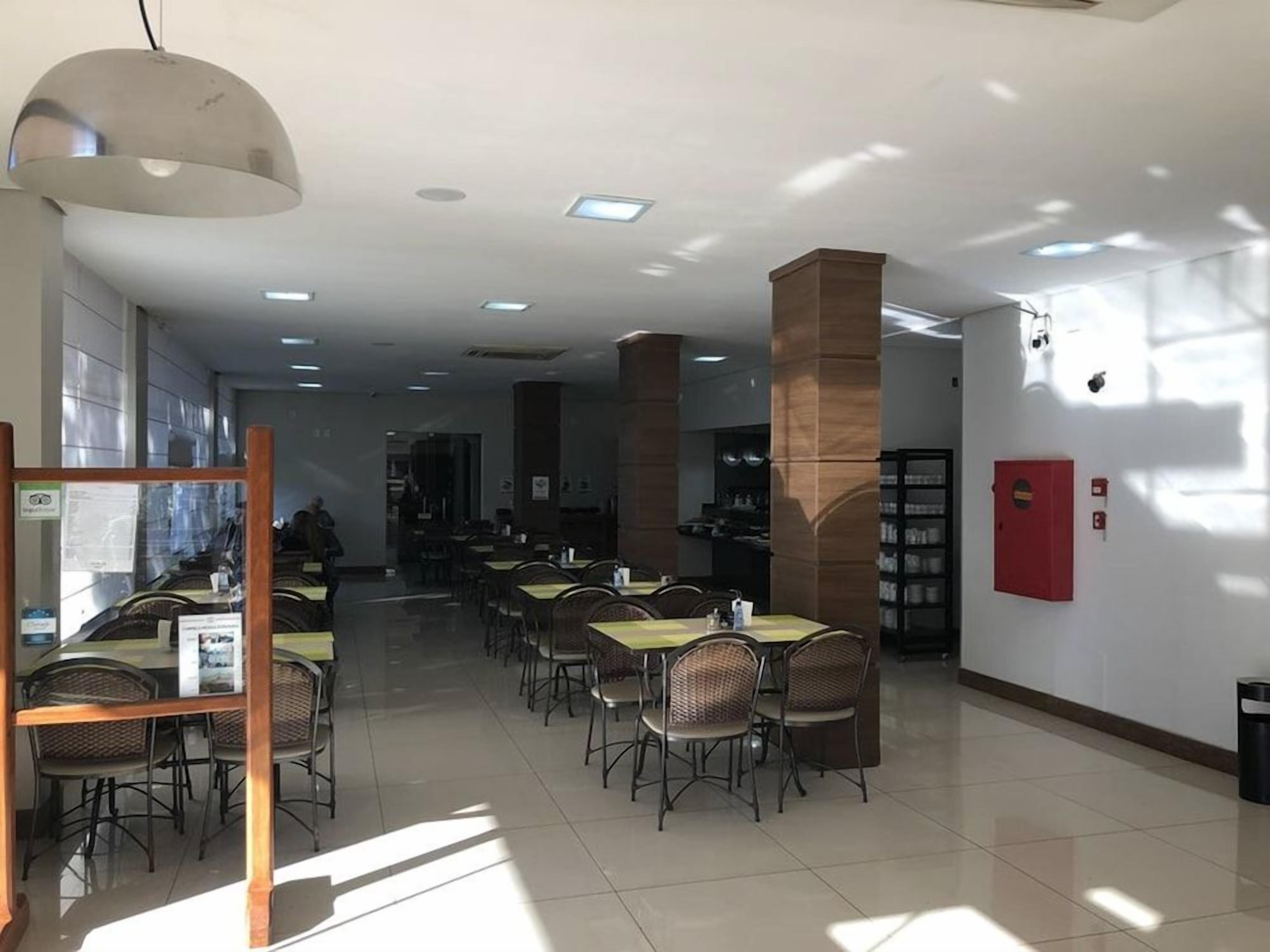 Um espaço amplo e interno com várias mesas e cadeiras, um lustre grande pendurado e um extintor de incêndio na parede.