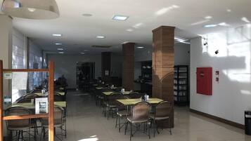 Um espaço amplo e interno com várias mesas e cadeiras, um lustre grande pendurado e um extintor de incêndio na parede.