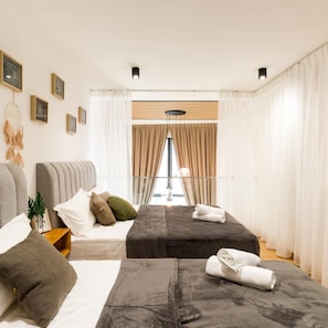 Habitación de hotel con dos camas, un ventanal con cortinas, una mesita de noche con lámpara y cuadros colgados en la pared.