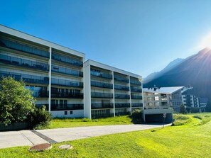 Ein mehrstöckiges Hotel mit Balkonen, einem Parkplatz und einem Berg im Hintergrund.