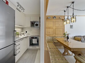 Eine moderne Küche mit Backofen, Kühlschrank und einem Essbereich mit Holztisch und Bank.