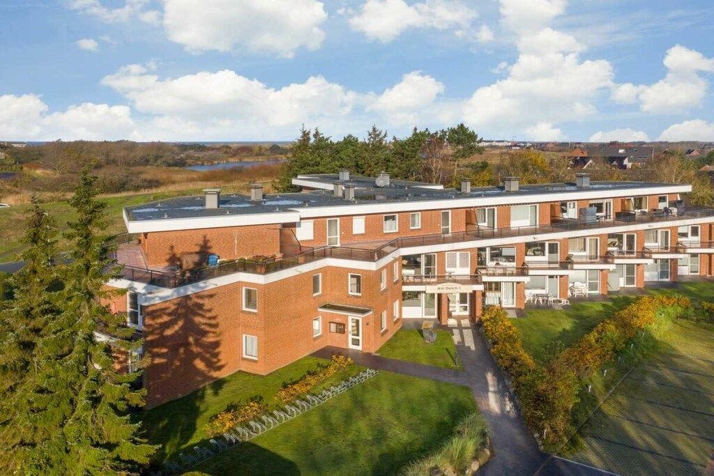 A multi-story residential building with a flat roof, large windows, and a well-maintained lawn.