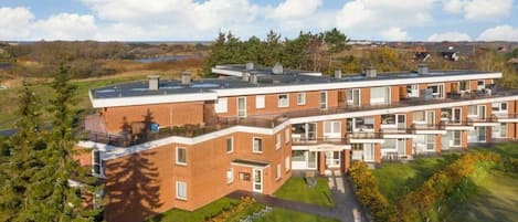Un edificio residencial de varios pisos con techo plano, ventanas amplias y un césped cuidado.