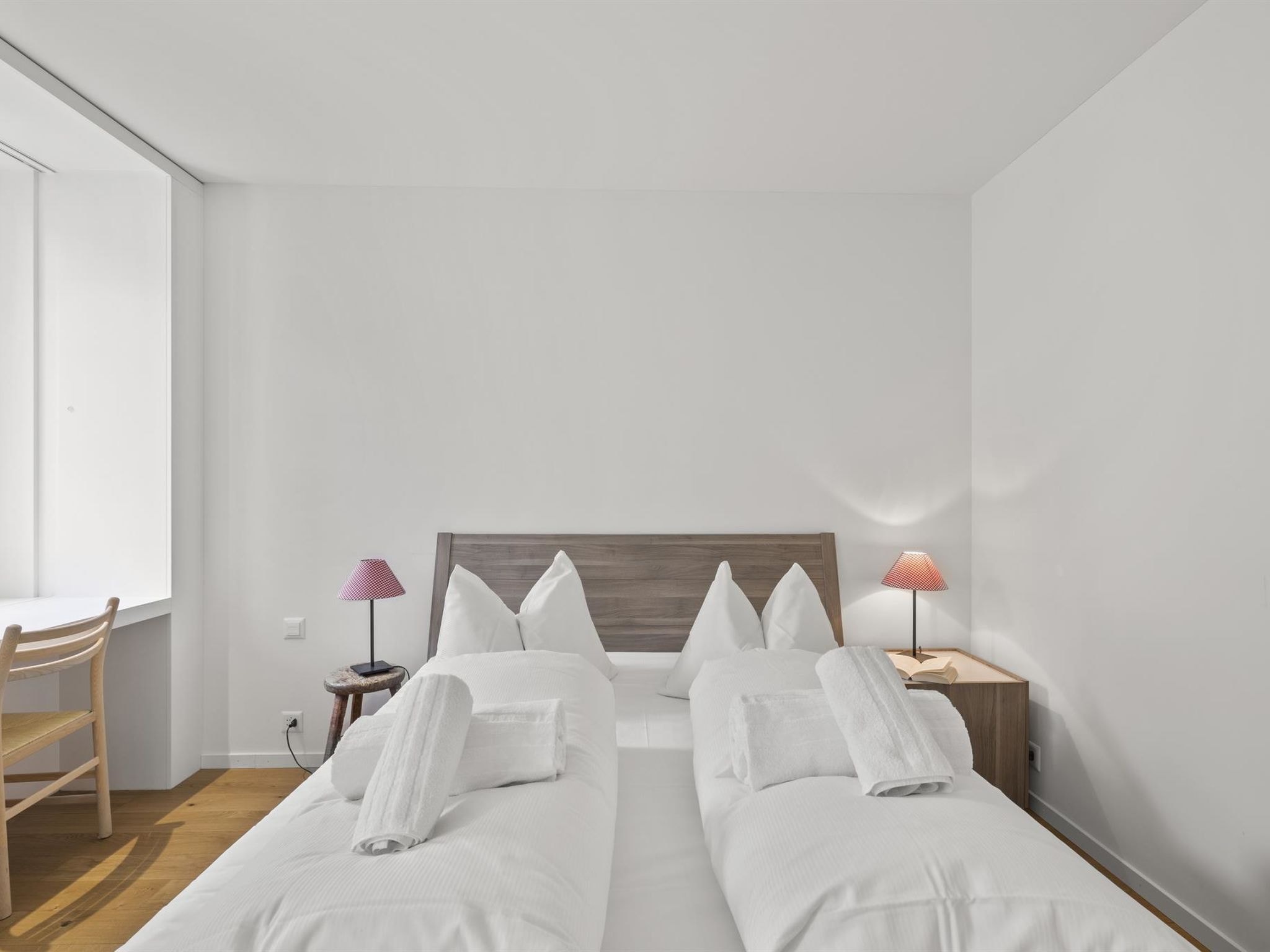 Una habitación de hotel con una cama doble, dos mesitas de noche, una silla y un ventanal.