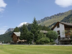 A mountain lodge with a wooden cabin and a white building, surrounded by lush greenery and mountains. - Triangel Raber Appartement/Fewo Triangel Raber IH by Interhome (Parpan)