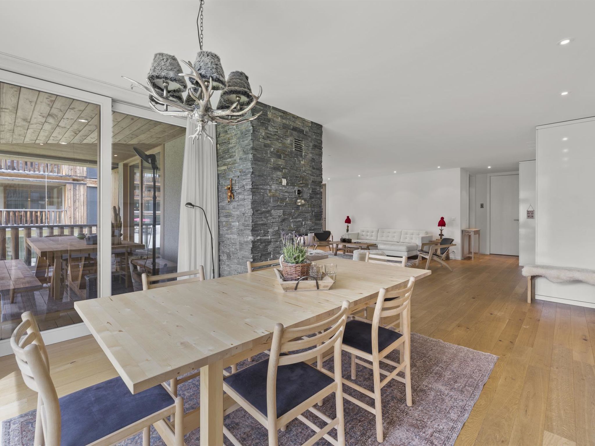 Ein moderner Essbereich mit einem Holztisch und -stühlen, einer Wand aus Stein und einer Glastür, die zu einem Außenbereich führt.
