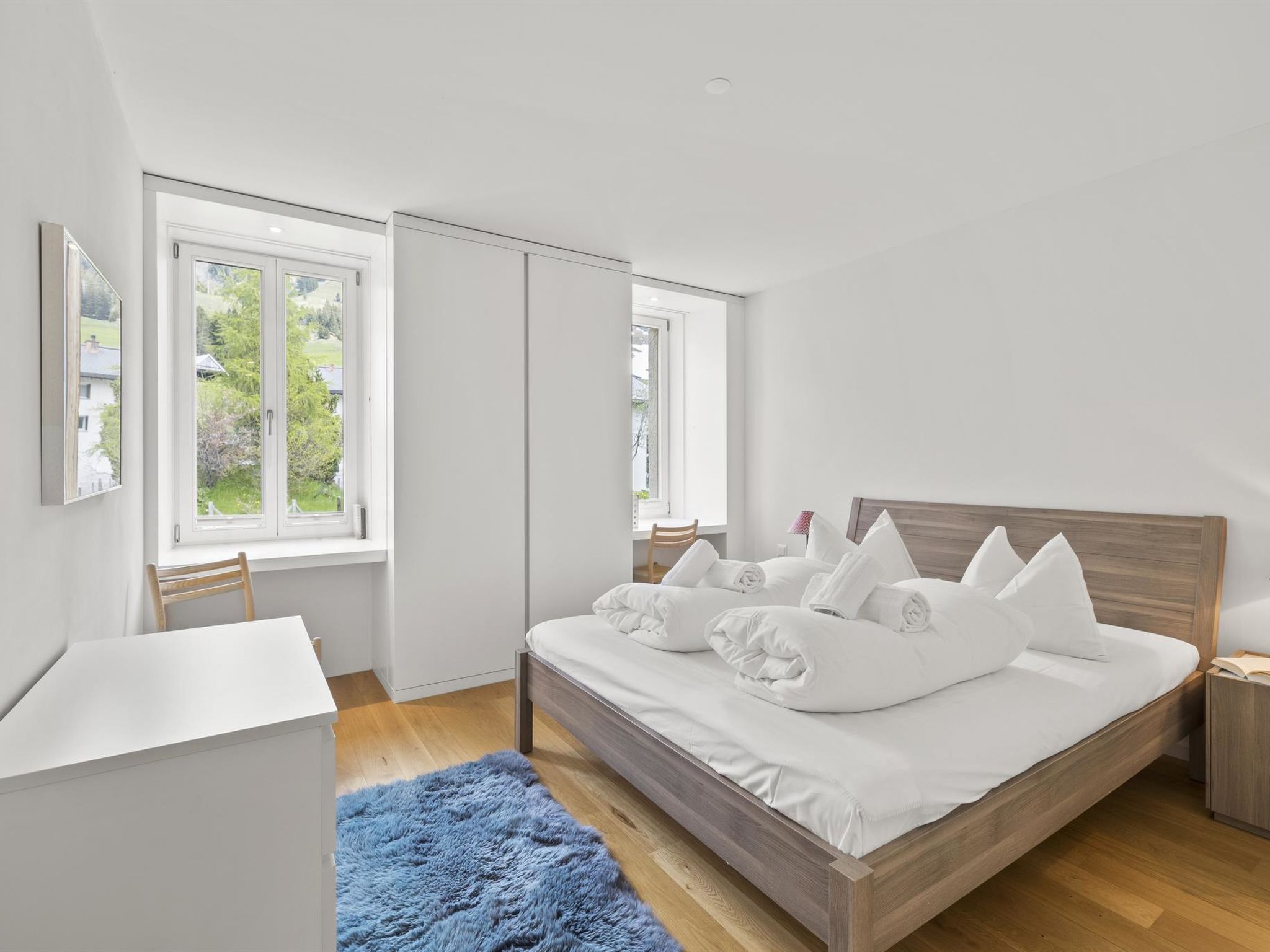 A modern bedroom with a large bed, a desk, and two windows.